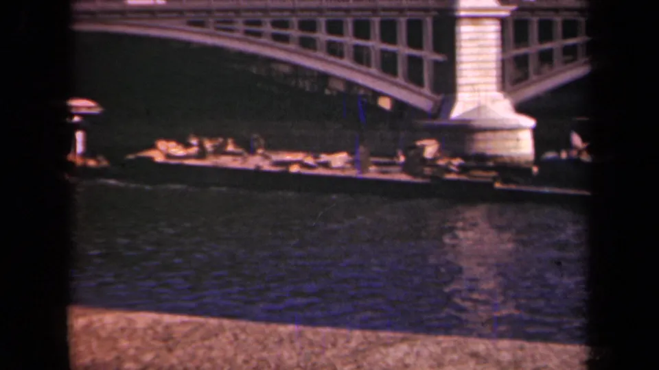 1939 Paris home-movie frame showing a bridge pier, arched span, and low river boat below.