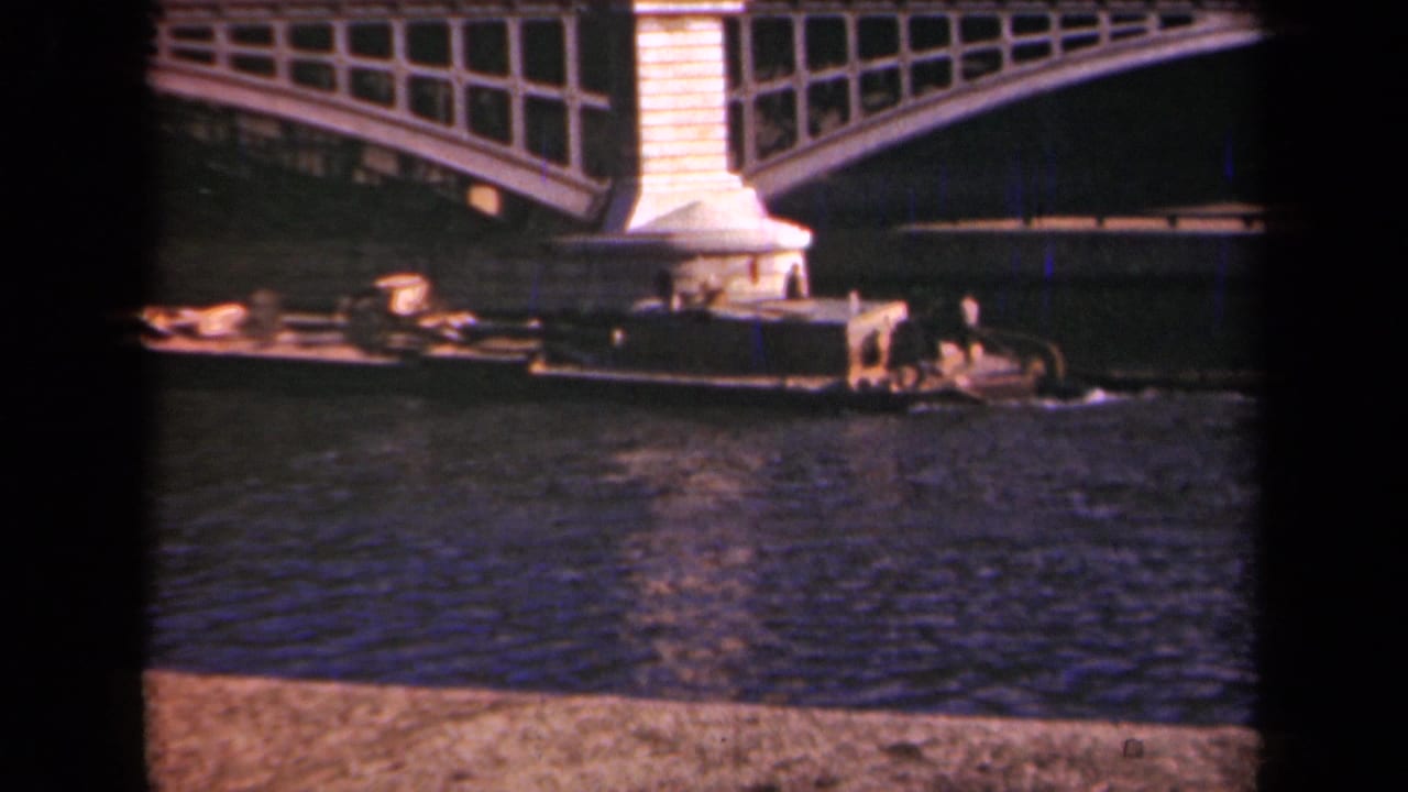 Work barge passing beneath a large arched bridge over the river.