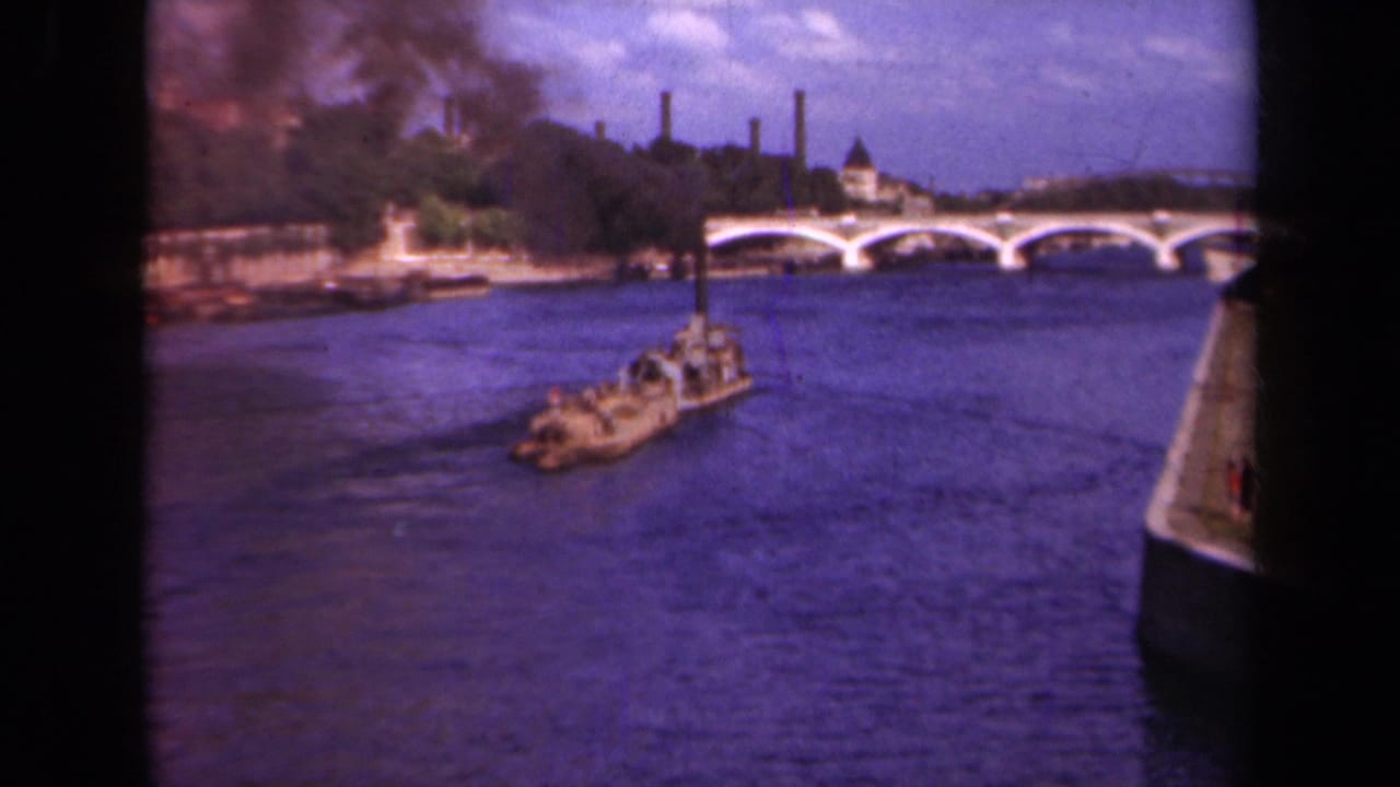 1939 Paris home-movie frame showing a barge on the Seine, a multi-arched bridge, smokestacks, and dark smoke near the riverbank.
