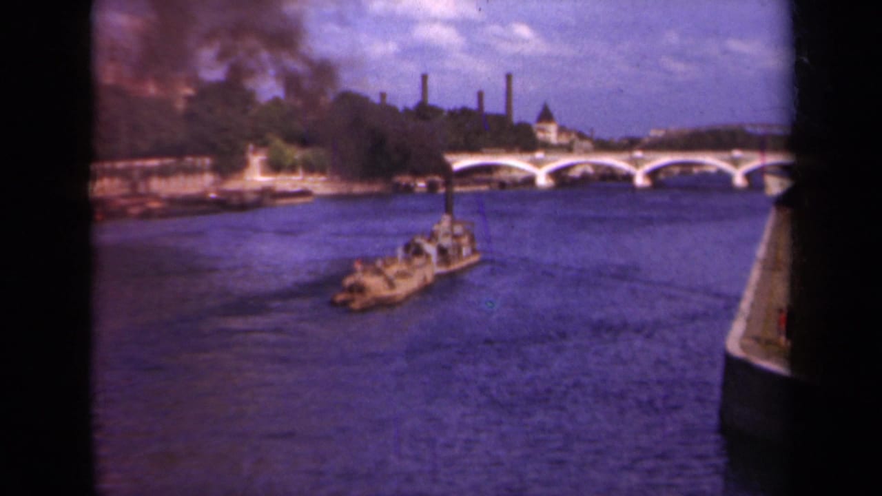 Paris, 1939, with a working barge on the Seine, smoke drifting above trees, and an arched bridge in the background.