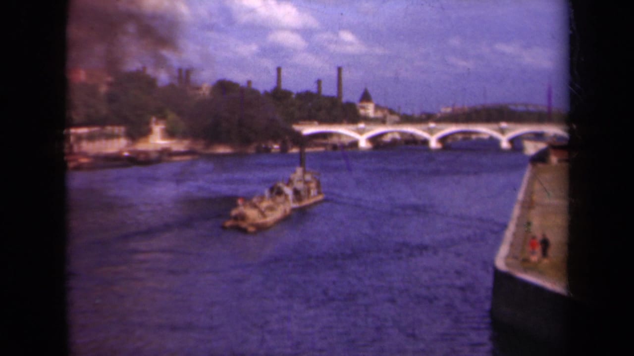 The Paris river view continues as the boat crosses blue water below the bridge, with the embankment and skyline in soft focus.