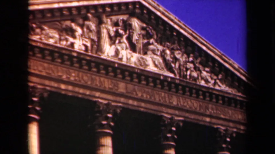 Paris architectural detail shows a sculpted pediment and column tops on a grand classical building against deep blue sky.