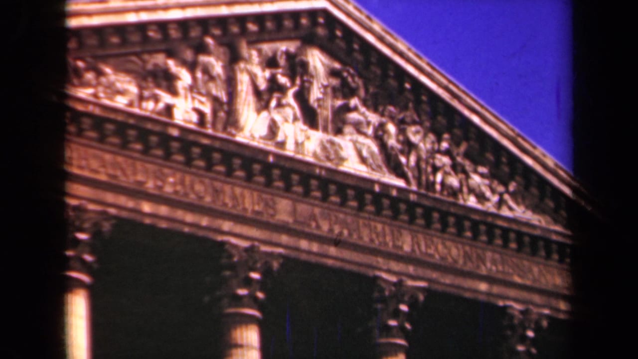 1939 Paris 8mm frame showing a classical pediment with carved human figures, columns, inscription band, and blue sky.