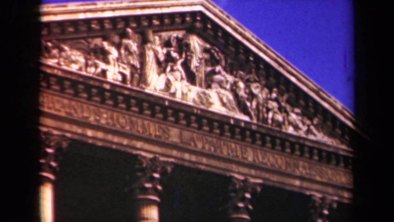 1939 Paris footage frames the carved pediment and inscription of a neoclassical monument above partial column capitals.