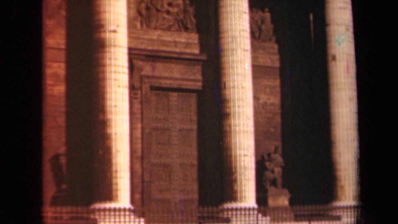 Close 8mm view of the Paris landmark facade with fluted columns, shadowed recesses, and carved stone ornament.