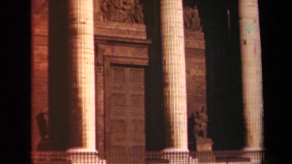 Close 8mm view of the Paris landmark facade with fluted columns, shadowed recesses, and carved stone ornament.
