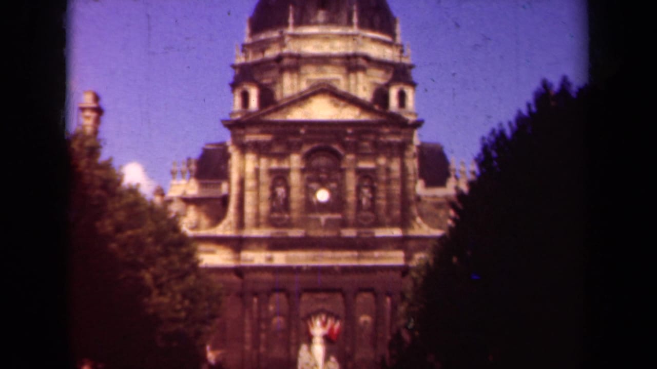 1939 Paris frame with a domed stone building centered between trees, the entrance area and small distant figures near the bottom.