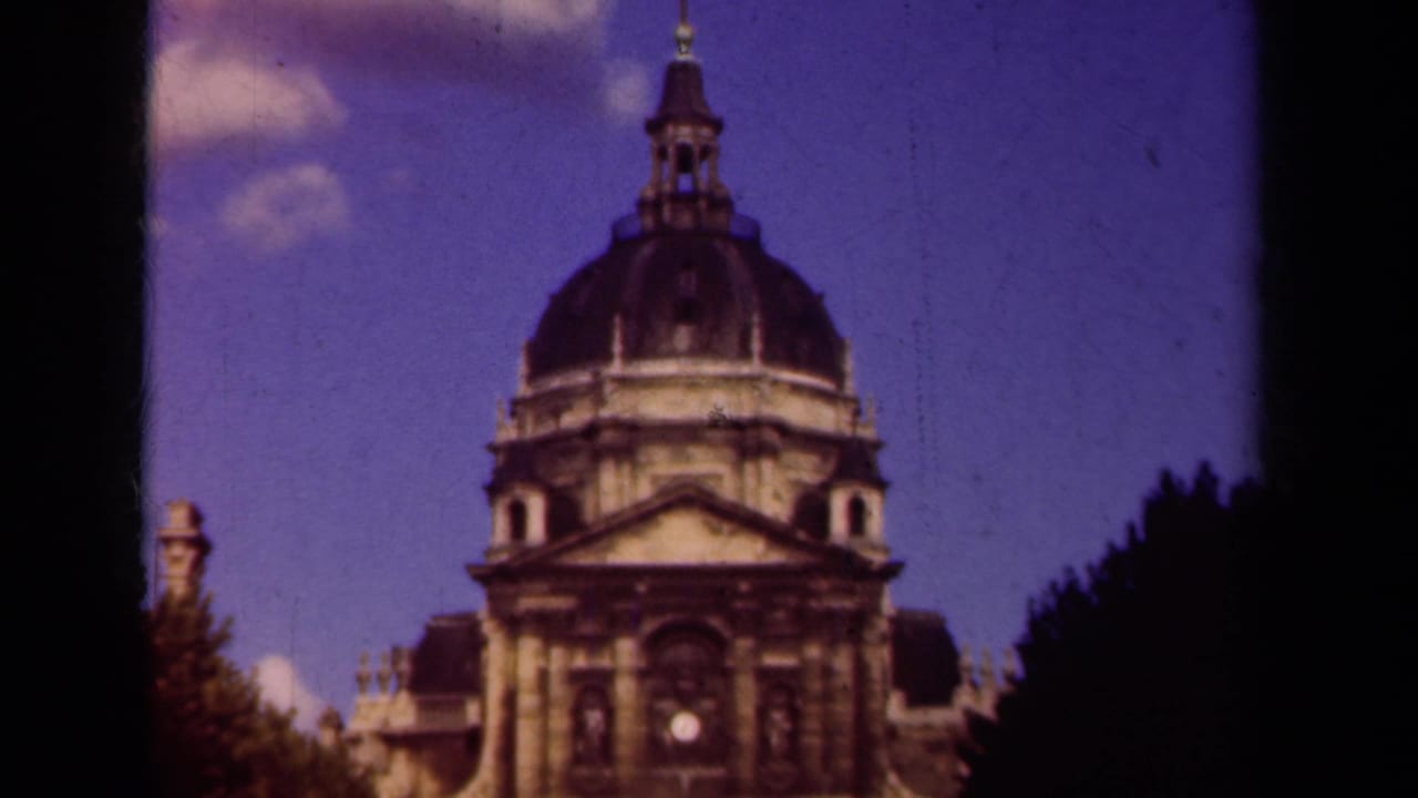1939 Paris home-movie frame showing a grand domed stone building viewed from above, with trees and a blue sky around it.