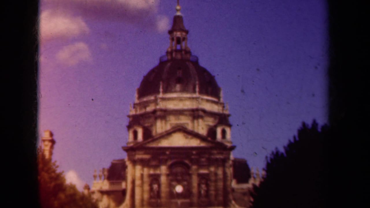 Soft 8mm frame of a domed Paris building with classical stone details, dark tree shapes, and visible film borders.