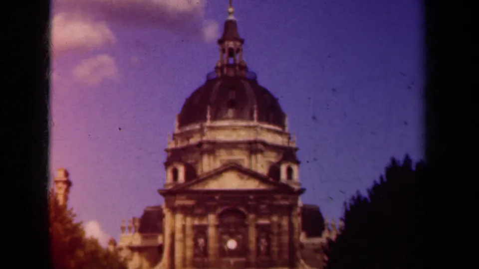 Soft 8mm frame of a domed Paris building with classical stone details, dark tree shapes, and visible film borders.