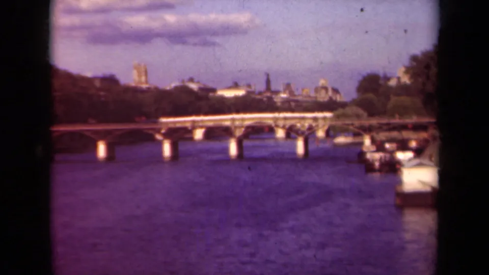 1939 Paris 8mm frame showing a Seine bridge, moored boats, trees, and distant Notre-Dame skyline through dark film borders.