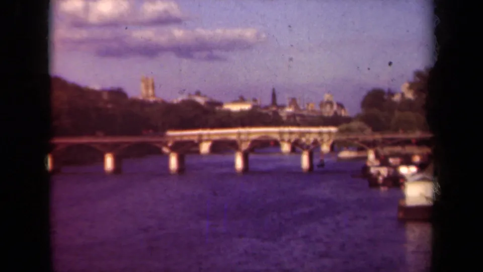 1939 Paris home-movie still with a Seine bridge, dark film borders, moored boats, and Notre-Dame towers in the distance.