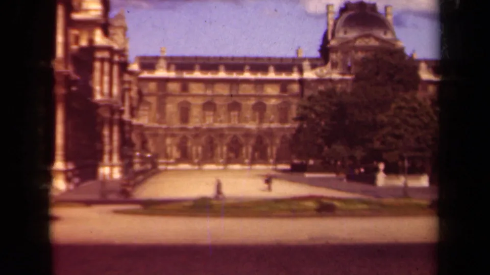 1939 Paris home-movie frame showing the Louvre facade, courtyard paving, garden beds, trees, and small figures in the distance.