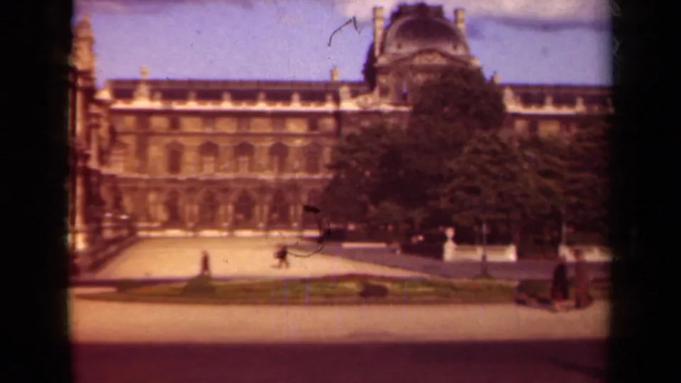 1939 Paris frame of the Louvre courtyard, showing the facade, trees, clipped garden beds, open paving, and pedestrians at the edge of the shot.