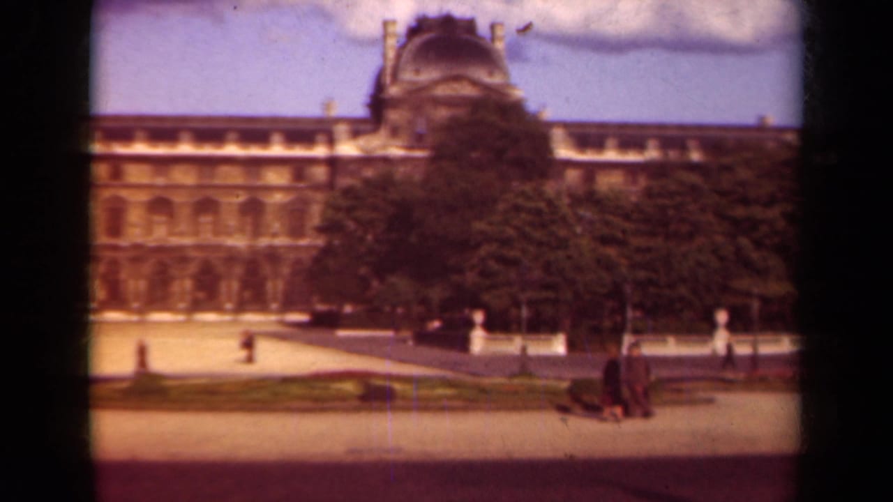 Louvre facade behind trees with pedestrians crossing a sunlit plaza.