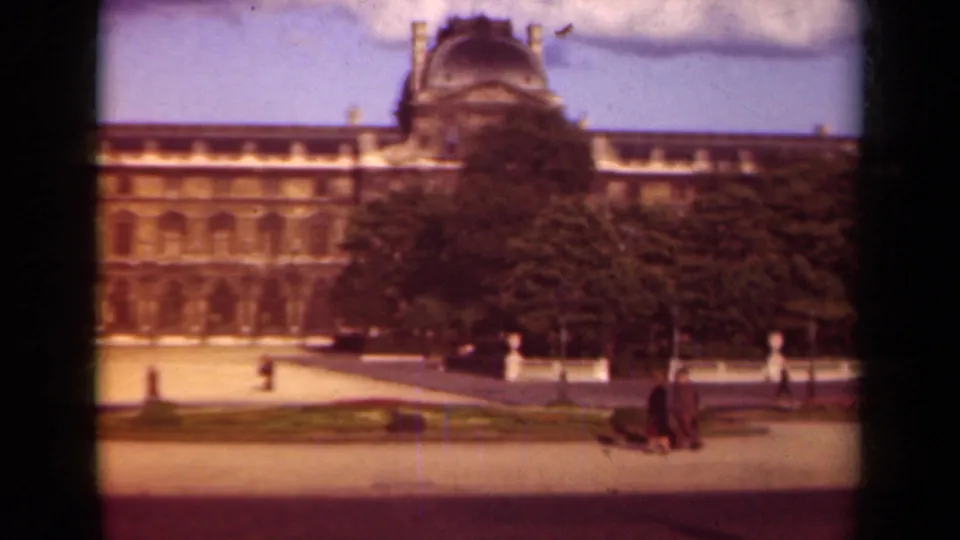 1939 Paris home-movie frame showing the Louvre facade, trees, paths, and pedestrians in a landmark courtyard.