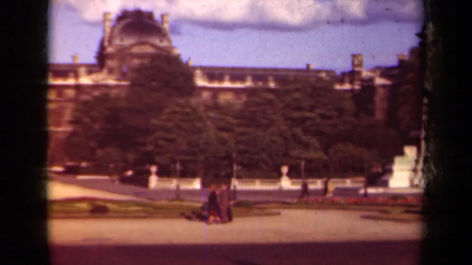 1939 Paris frame with the Louvre facade partly screened by trees as pedestrians move through the courtyard.