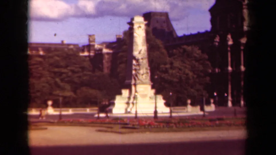 1939 Paris frame with the monument slightly closer, bordered by trees and red flowerbeds, with lampposts, walkway, distant people, and a dark car visible.