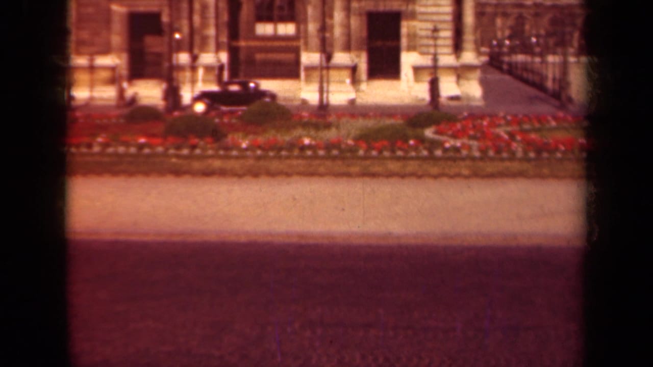 Black car continues along the street beside a planted median and ornate building frontage.