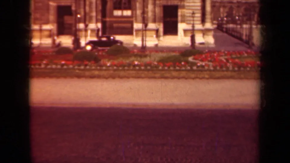 The car appears farther along the Paris street, with red flowers, iron railings, and a formal stone entrance behind it.