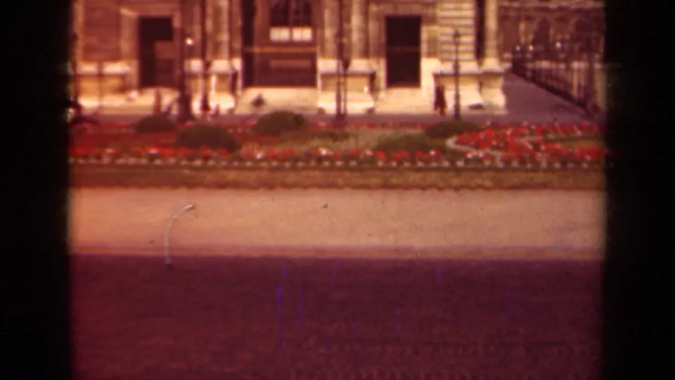 A 1939 Paris street frame shows distant pedestrians near a curb, red flower beds, a stone facade, and visible 8mm frame edges.