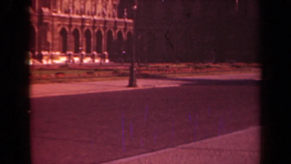 1939 Paris frame with a historic arched facade, lamppost, landscaped strip, trees, and broad pavement seen from a fixed viewpoint.