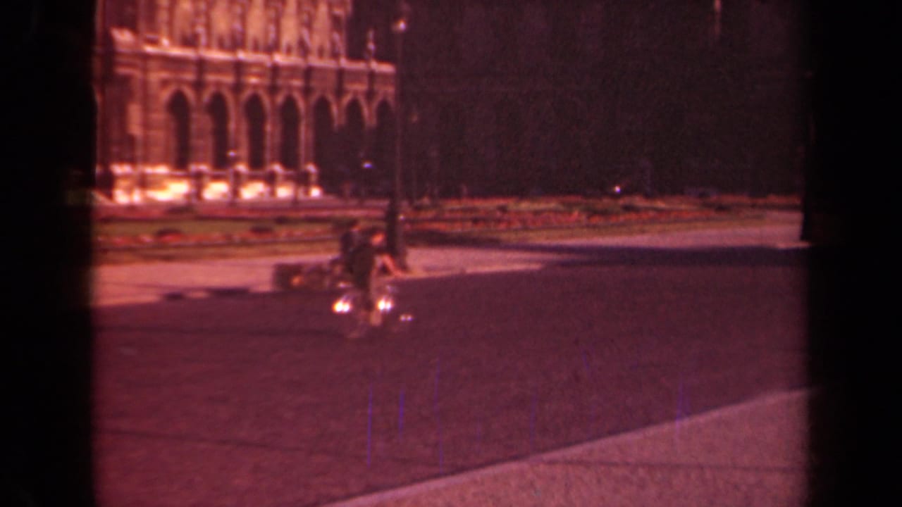 1939 Paris frame with a bicyclist riding through an open square, backed by a lamppost and illuminated arched facade.