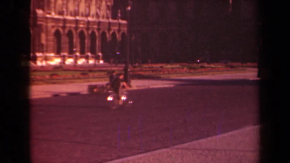 1939 Paris frame with a bicyclist riding through an open square, backed by a lamppost and illuminated arched facade.
