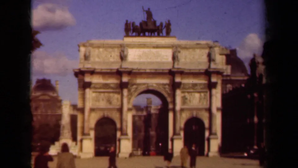 1939 Paris home-movie frame showing a triumphal arch with quadriga sculpture and pedestrians in the foreground.
