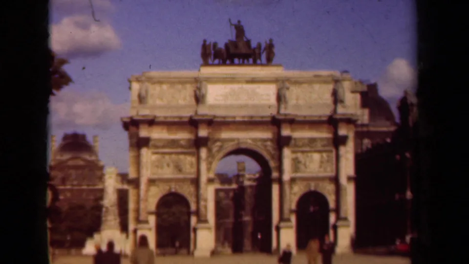 1939 Paris home-movie view of the Arc de Triomphe, framed softly with small pedestrians and dark film edges.