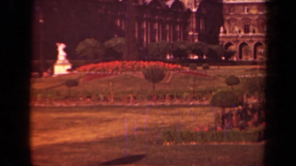 Paris garden view near the Louvre, showing red flowerbeds, shaped greenery, a white statue, and historic architecture beyond.
