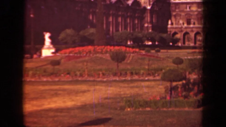 1939 Paris home-movie frame of a formal garden near the Louvre, with red flowers, clipped shrubs, lawn, and a white statue.