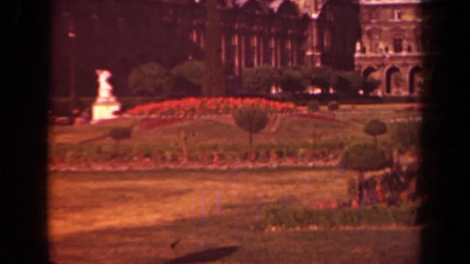 1939 Paris home-movie frame with soft focus on a formal garden, including a white statue, red flowerbeds, grass, shrubs, and stone facade.