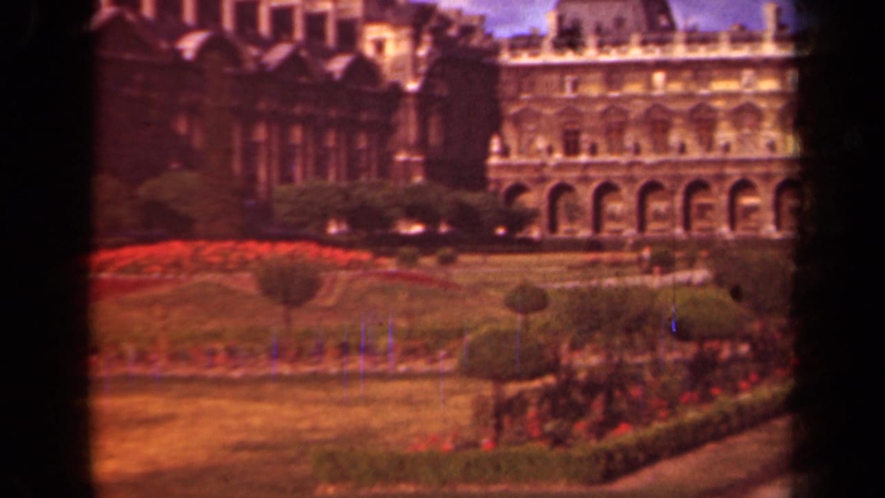 1939 Paris home-movie view of the Louvre facade with arched colonnades, lawns, hedges, and red flowerbeds.