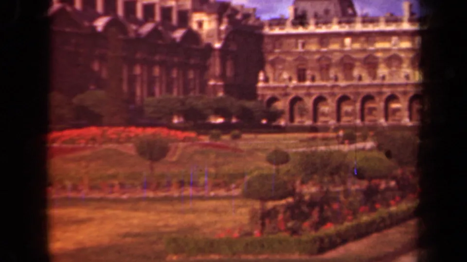1939 Paris home-movie view of the Louvre facade with arched colonnades, lawns, hedges, and red flowerbeds.