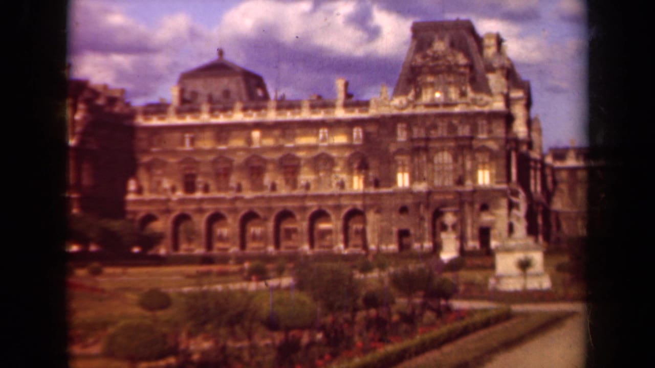 1939 Paris 8mm view of the Louvre palace facade, arched ground level, formal garden beds, and a partly cloudy sky.