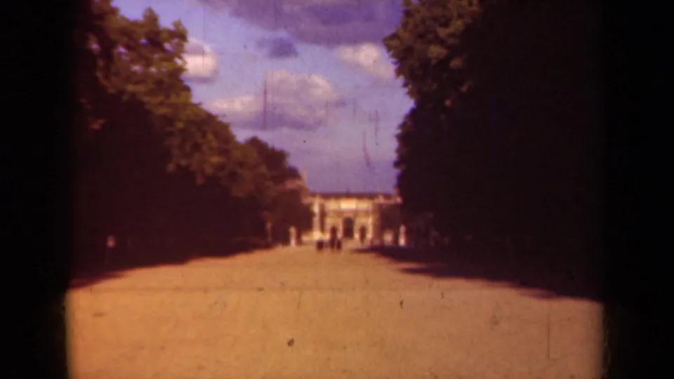 Soft 8mm frame of a Paris park promenade in 1939, with deep tree shade and a pale building at the end.