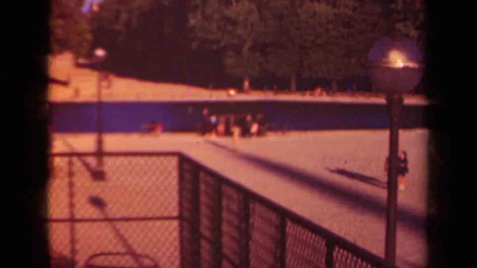 1939 Paris park poolside view with chain-link fencing, lampposts, trees, and small visitors around the water.