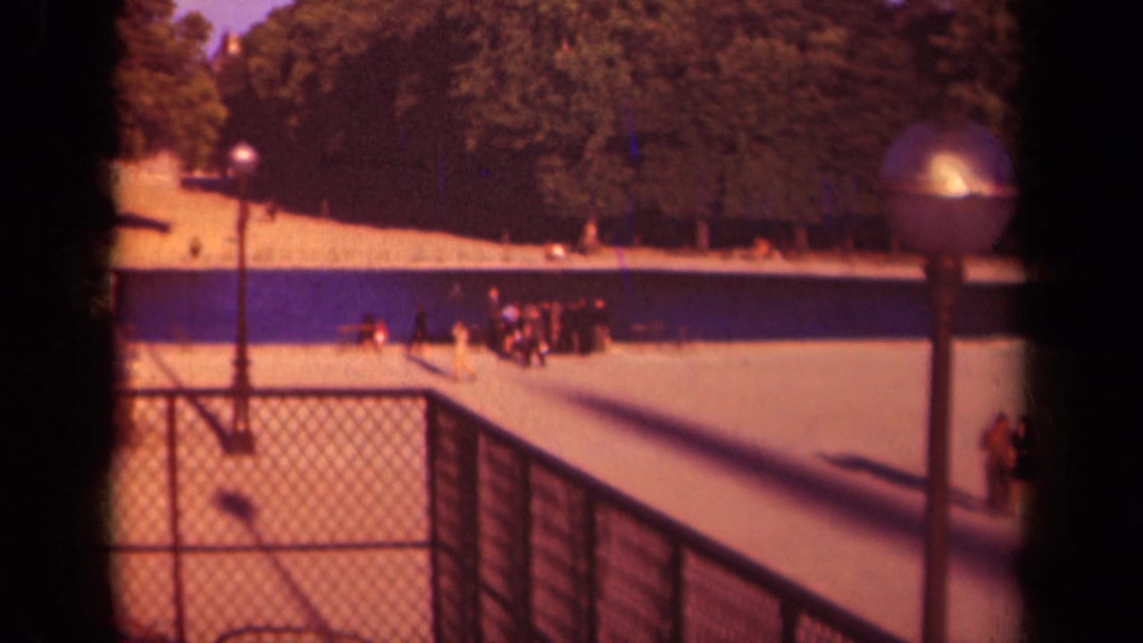 1939 Paris 8mm frame showing a raised view toward trees, a railing, a globe lamp, and small pedestrians near a formal park approach.