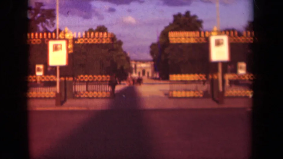 1939 Paris 8mm frame of ornate open park gates, posted signs, trees, and a path leading toward a distant building.