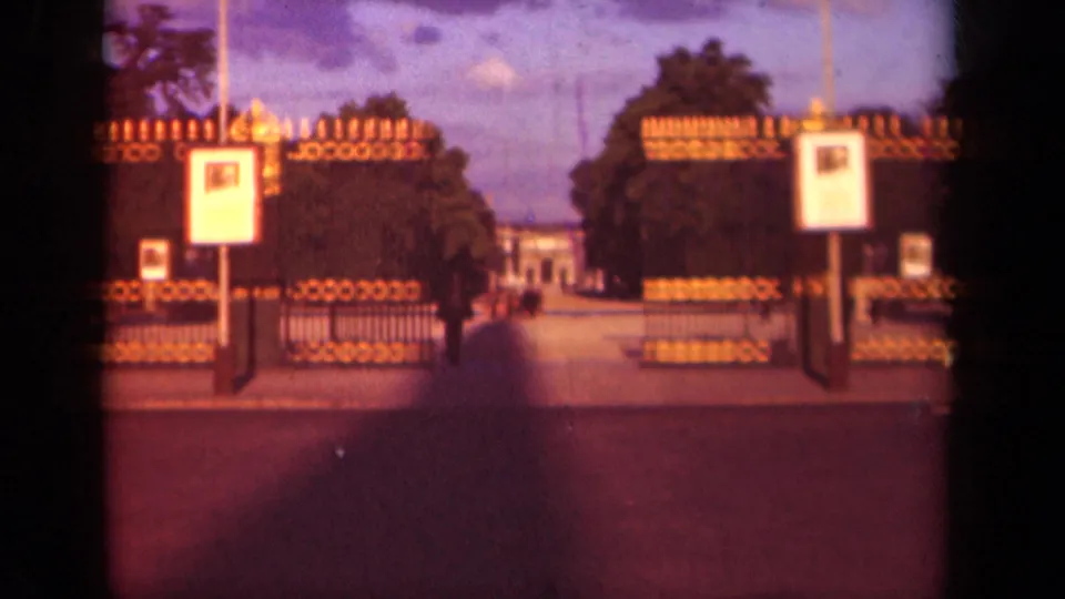 1939 Paris 8mm frame showing a formal gated park entrance with trees, signs, a central path, and distant pedestrians.
