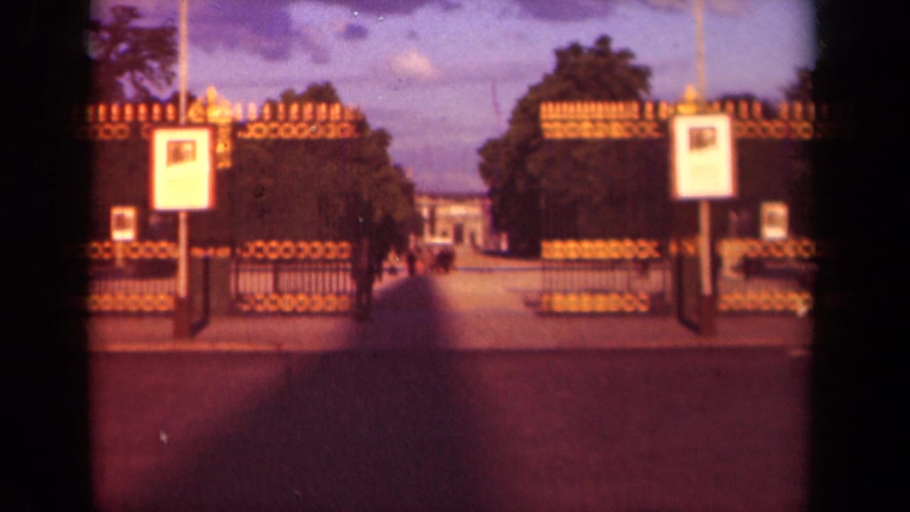Gate entrance with signboards, trees, walkway, and small figures in the distance.