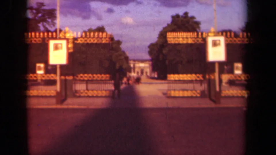 Soft 1939 Paris 8mm frame showing a gated walkway, trees, white signs, and blurred pedestrians near the entrance.