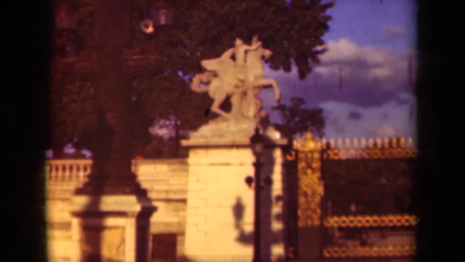 1939 Paris 8mm frame showing a pale equestrian statue on a stone pedestal, framed by trees, railings, a lamppost, and warm evening light.