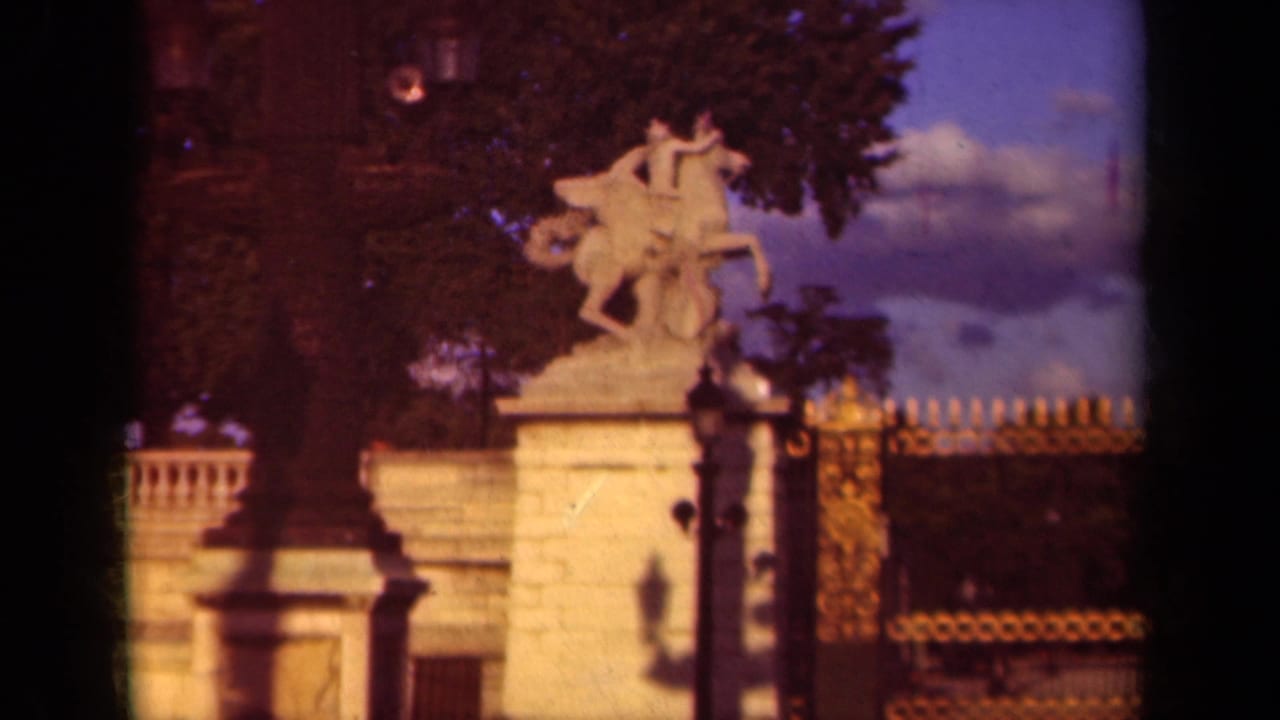 Equestrian stone statue on a pedestal near a decorative fence and trees.