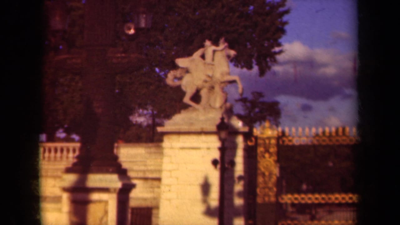 Equestrian statue and stone pedestal beside a dark fence and trees.