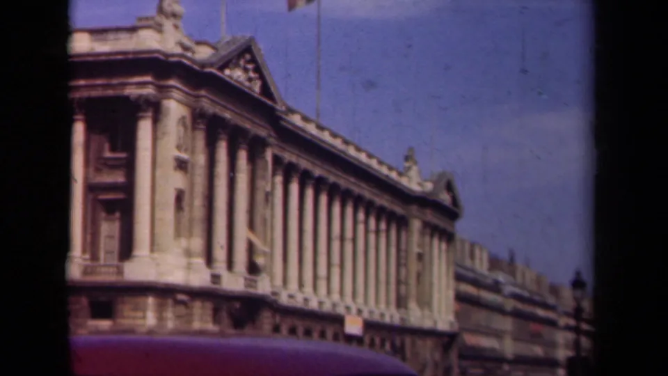 1939 Paris home-movie frame showing a grand stone building with tall columns, roof sculptures, and blue sky.