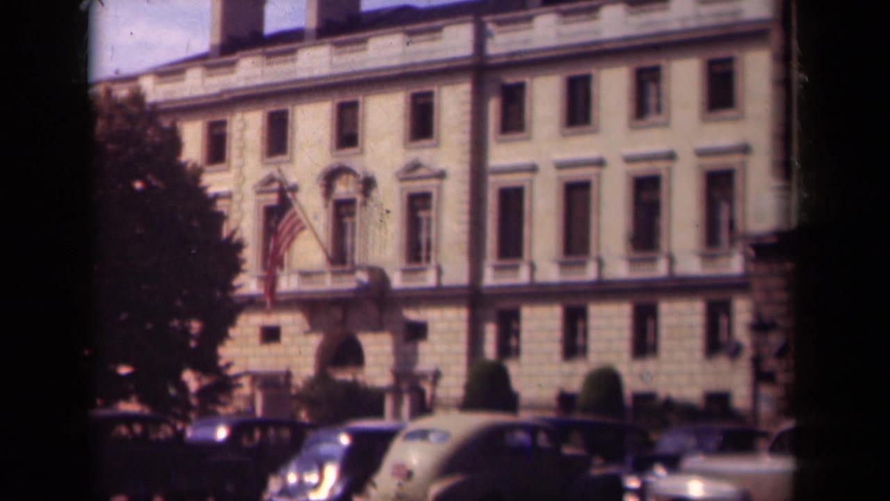 Classical stone building with American flag and parked 1930s cars along the street.