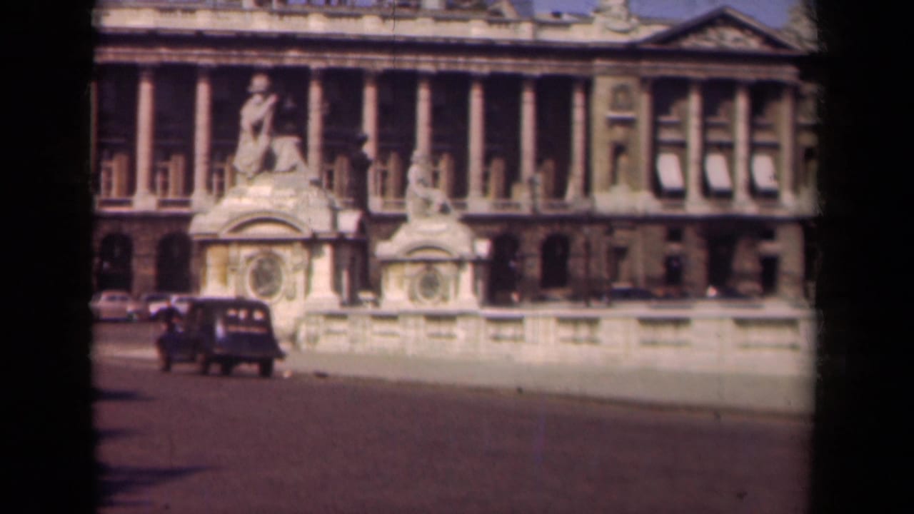 1939 Paris frame with a dark automobile passing a monumental stone facade, pedestrians, and parked period cars.