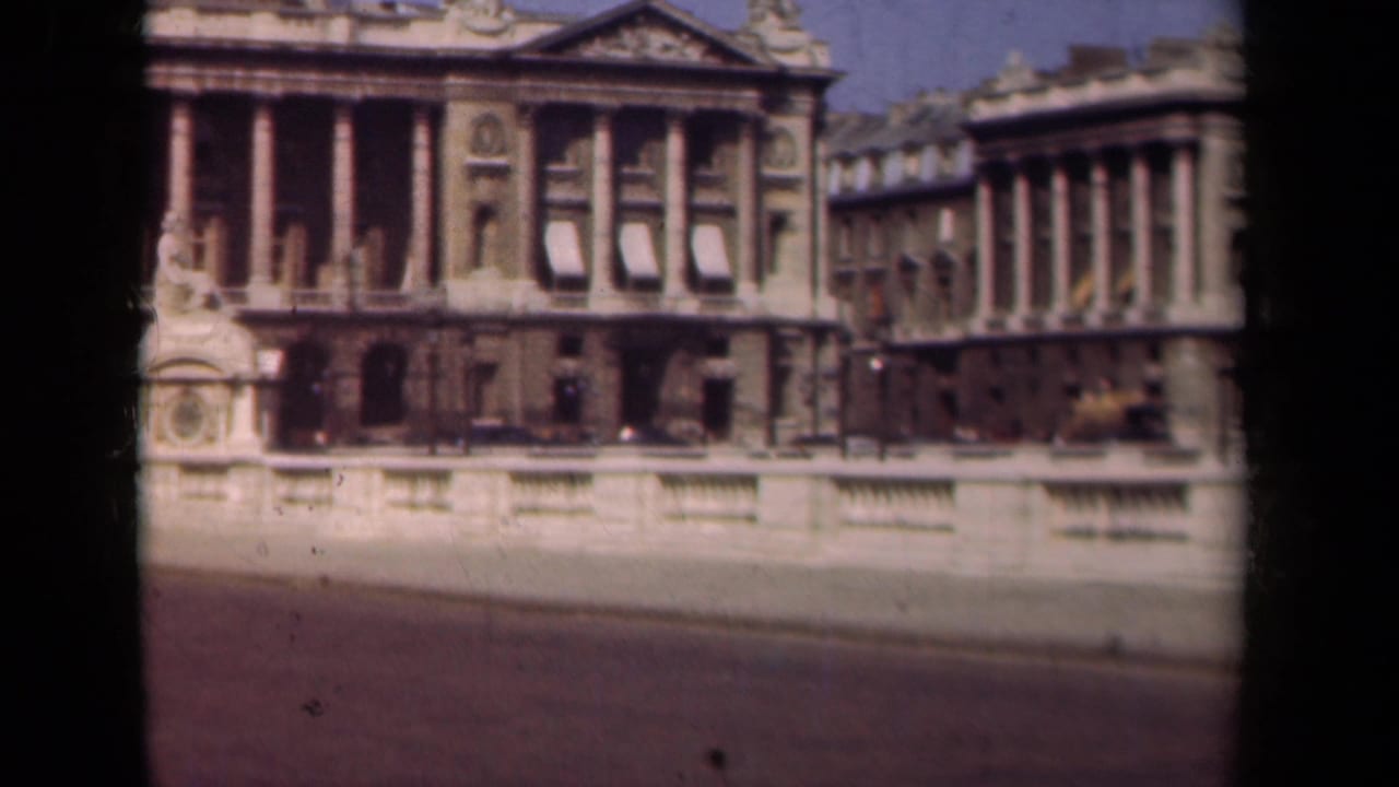 1939 Paris home-movie frame showing a classical building with columns, pediment details, and a stone bridge or terrace balustrade in front.